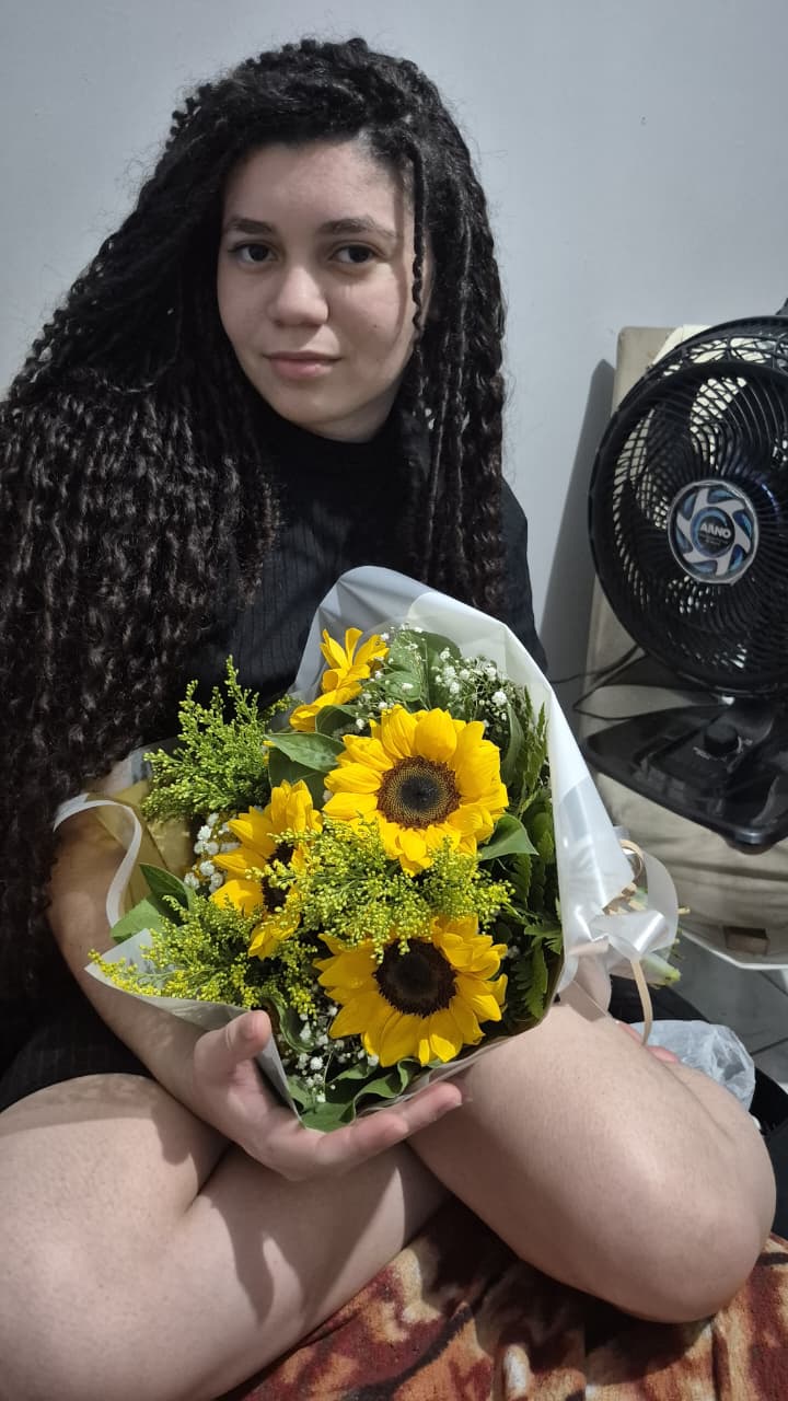Ela sentada segurando um buquê de girassóis