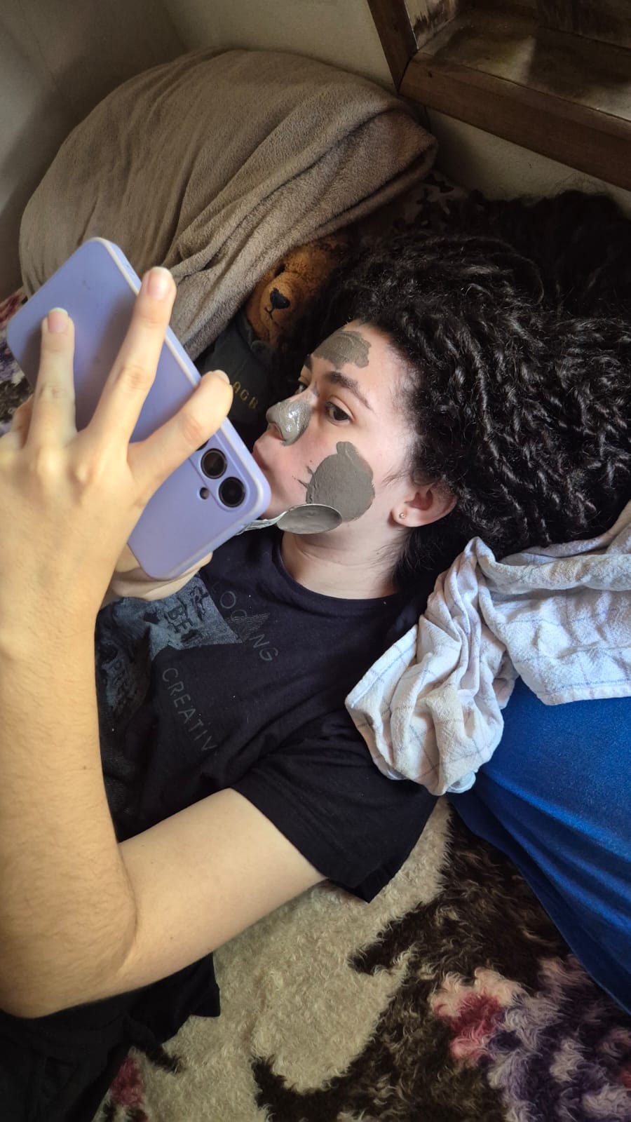 Ela deitada com máscara facial e o celular na mão